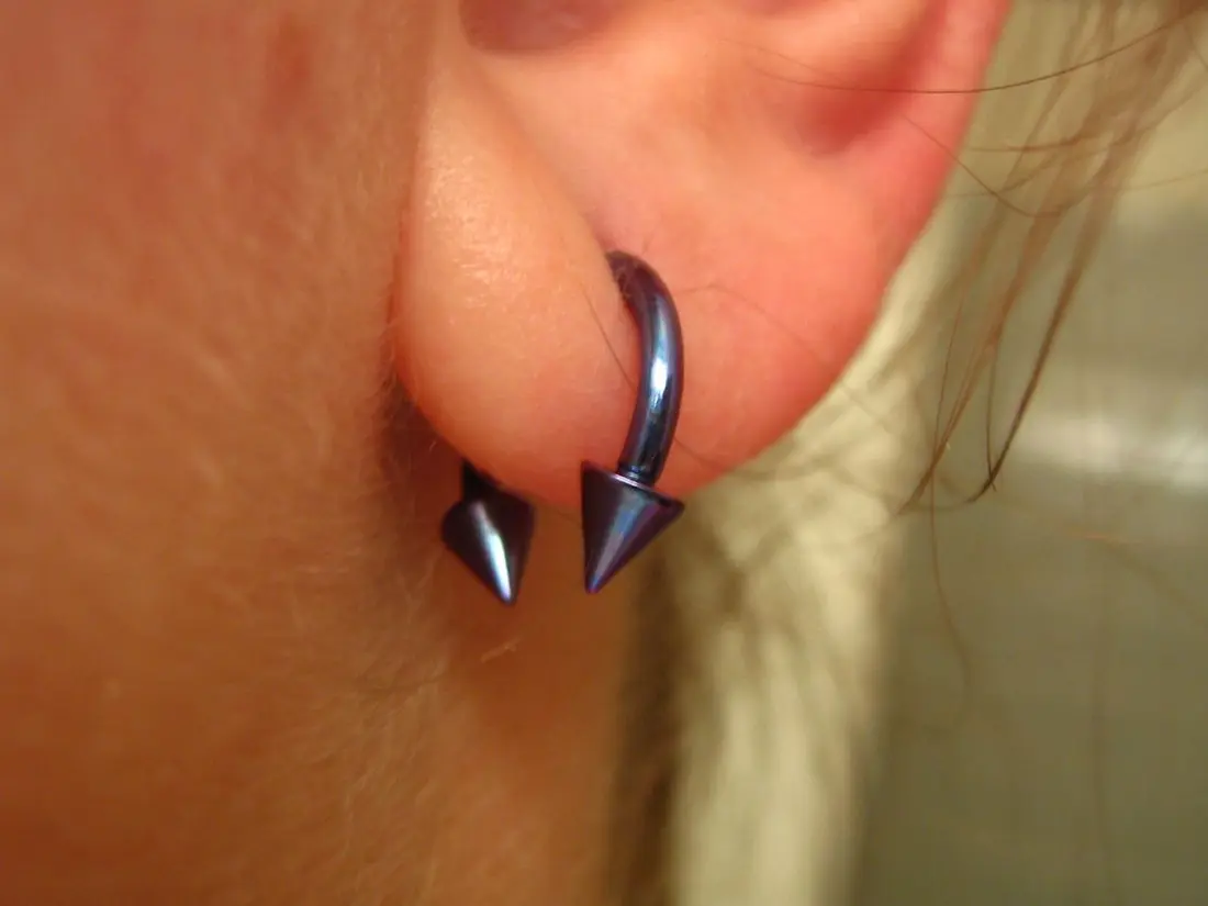 A dark circular barbell with cone ends worn through an ear piercing, the C-shaped bar clearly visible