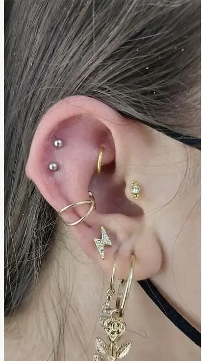Two silver studs stacked one above the other on the upper outer helix, with a conch cuff and lobe earrings below