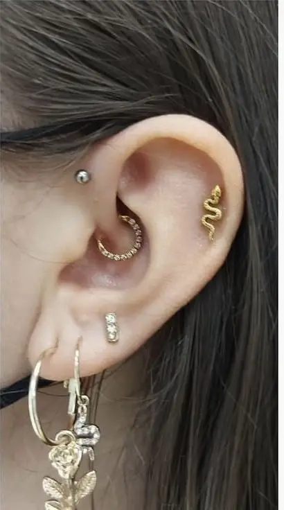 A gold snake-shaped stud in the flat cartilage of the upper ear, between the helix rim and the antihelix