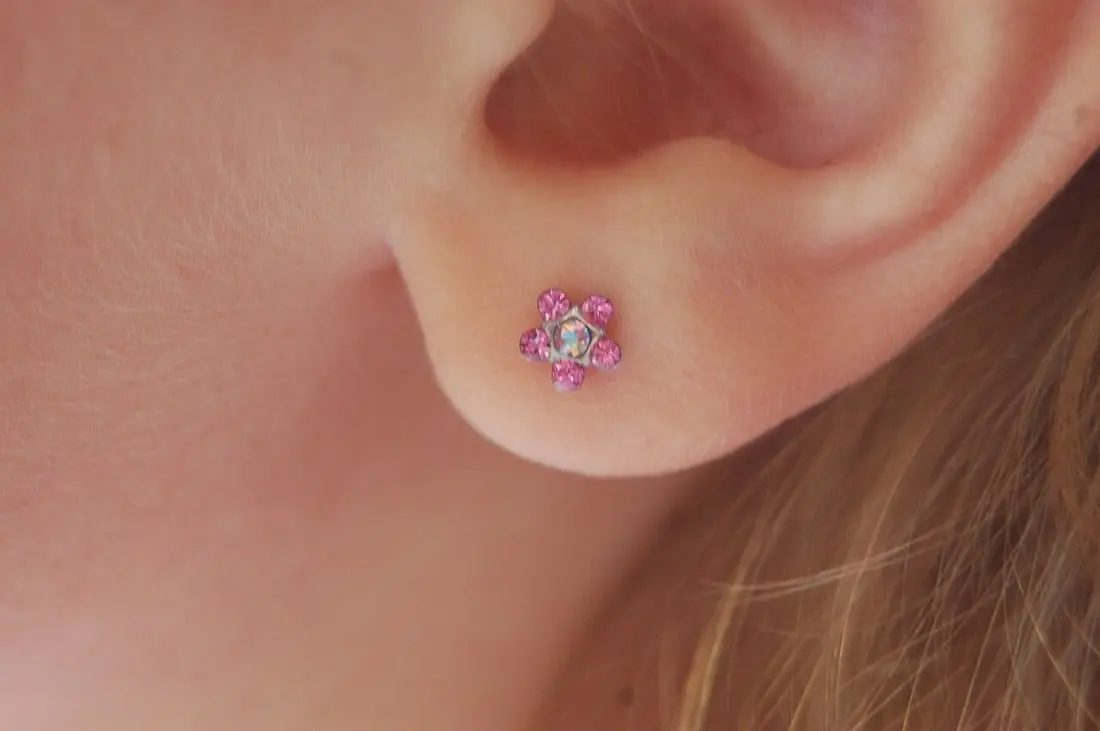 A freshly pierced earlobe with a pink crystal flower starter stud