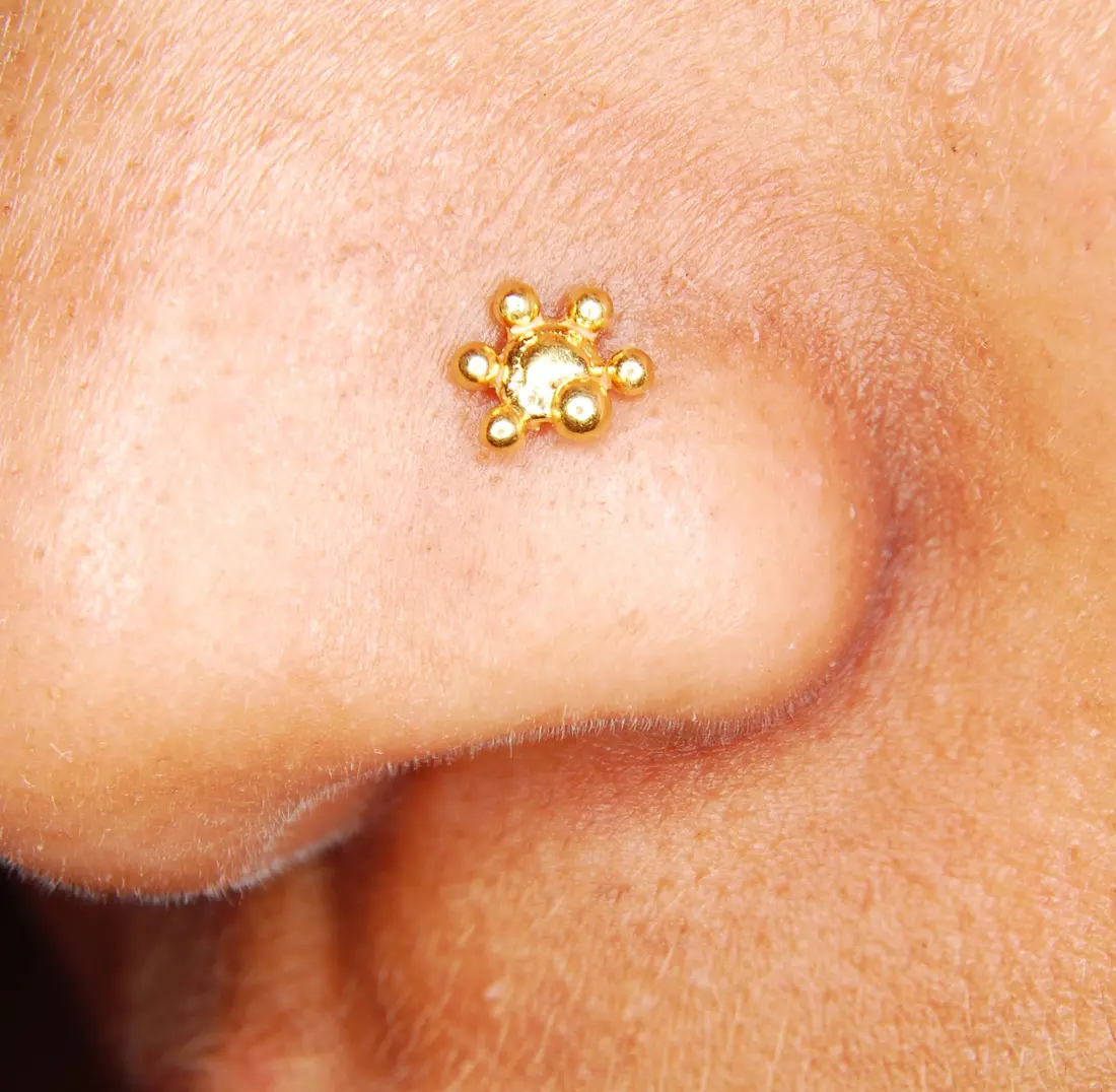 A decorative gold flower stud in a healed nostril piercing