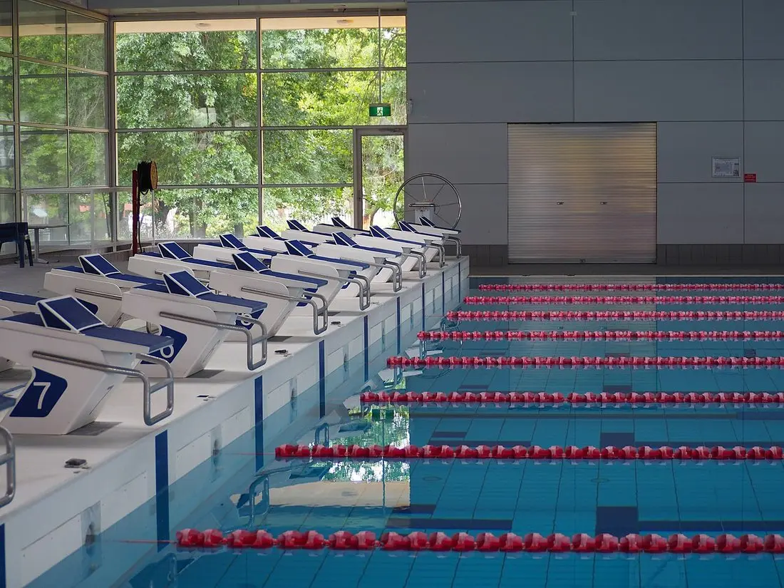 An empty indoor public swimming pool with lane ropes and starting blocks
