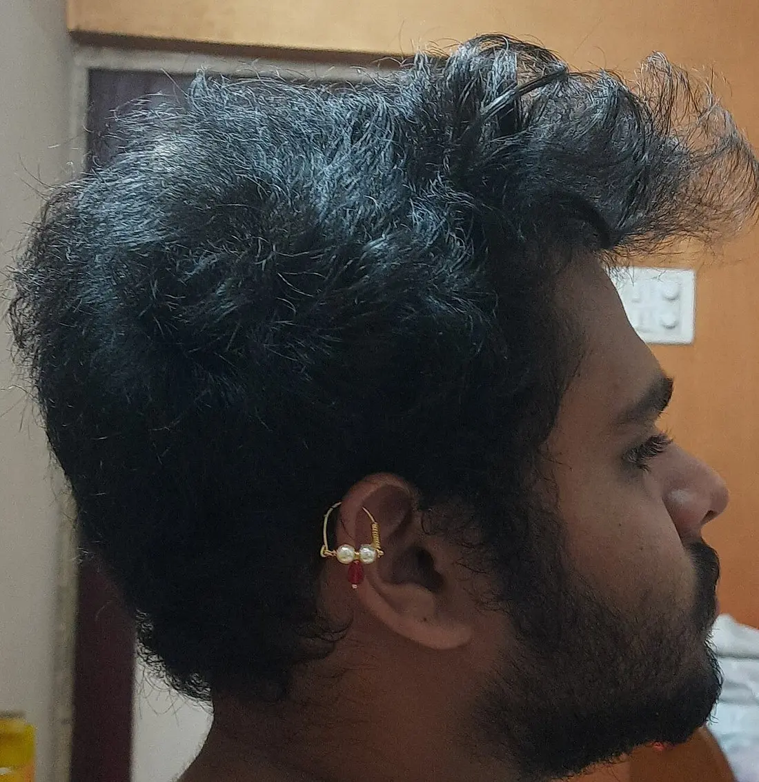 A bearded man in profile wearing a gold bhikbali ring with pearls through his upper ear