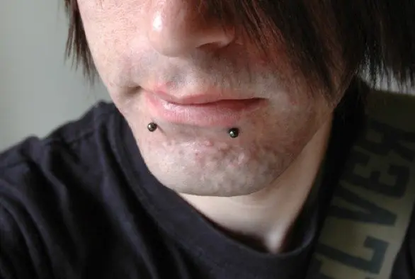 Two black ball studs below the lower lip, one near each corner of the mouth