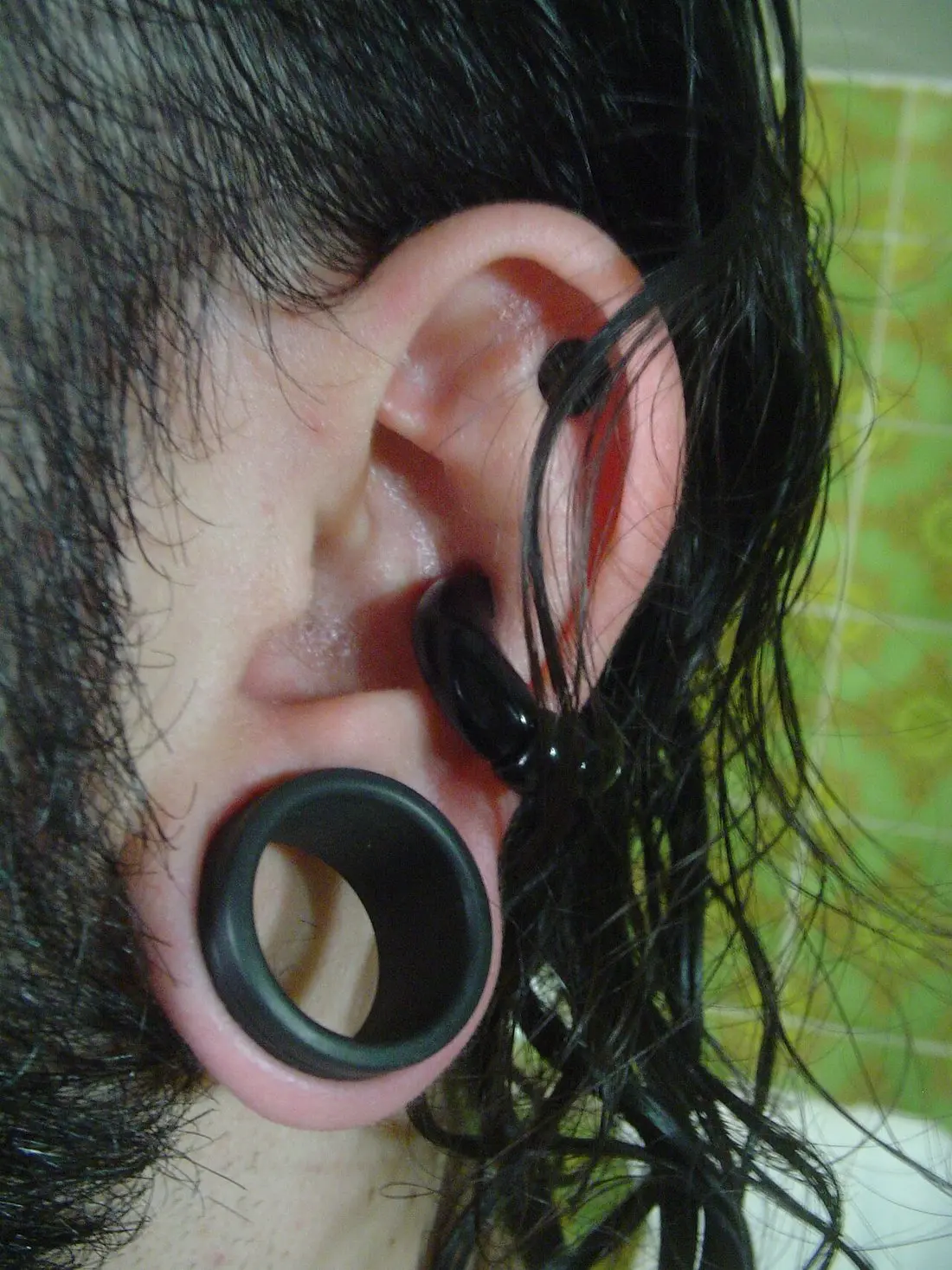 A stretched earlobe wearing a black flesh tunnel, with a larger ring in the conch above