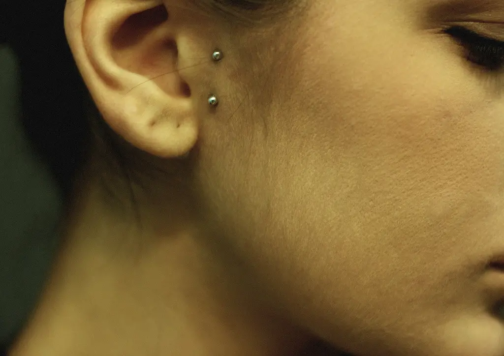 Two small bar ends sitting on the flat skin in front of the ear, the surface bar itself hidden beneath